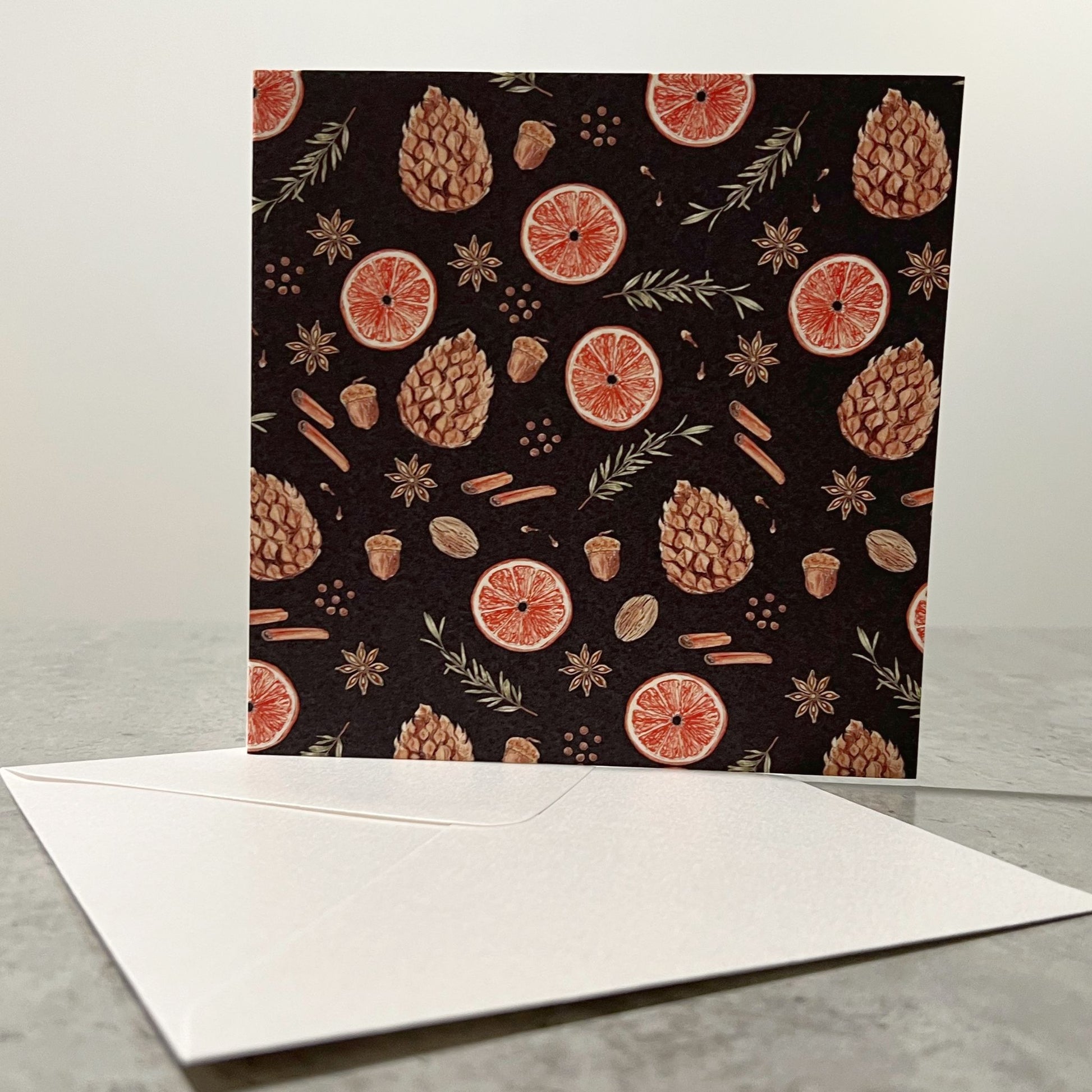 Greeting card with autumn-themed design featuring pinecones, acorns, and leaves on a dark background, accompanied by a white envelope.